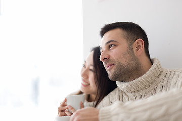 Image showing multiethnic couple enjoying morning coffee by the window