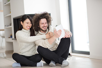 Image showing multiethnic couple using tablet computer in front of fireplace