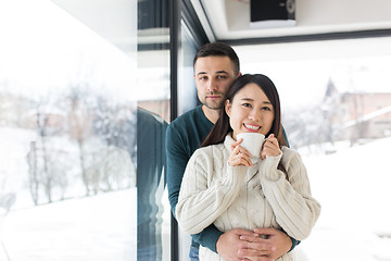 Image showing multiethnic couple enjoying morning coffee by the window