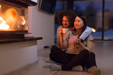 Image showing happy multiethnic couple sitting in front of fireplace