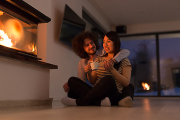 Image showing happy multiethnic couple sitting in front of fireplace