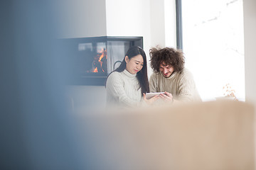 Image showing multiethnic couple using tablet computer in front of fireplace