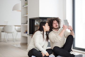 Image showing multiethnic couple using tablet computer in front of fireplace