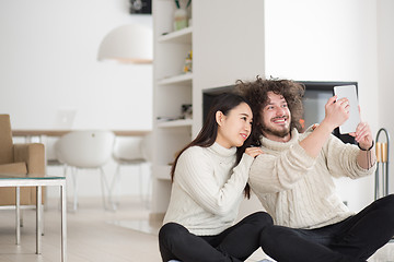 Image showing multiethnic couple using tablet computer in front of fireplace