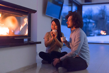 Image showing happy multiethnic couple sitting in front of fireplace