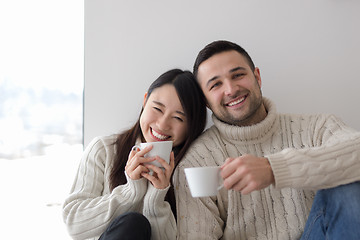 Image showing multiethnic couple enjoying morning coffee by the window