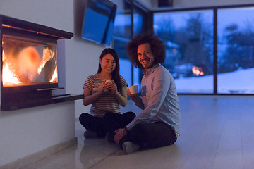 Image showing happy multiethnic couple sitting in front of fireplace