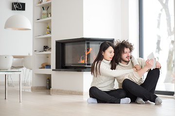 Image showing multiethnic couple using tablet computer in front of fireplace