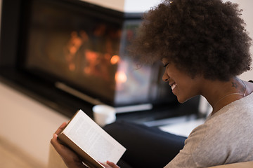 Image showing black woman reading book  in front of fireplace