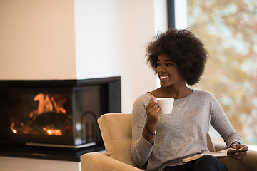 Image showing black woman reading book  in front of fireplace