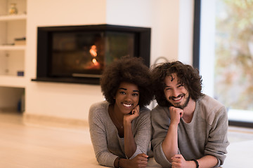 Image showing multiethnic couple lying on the floor  in front of fireplace