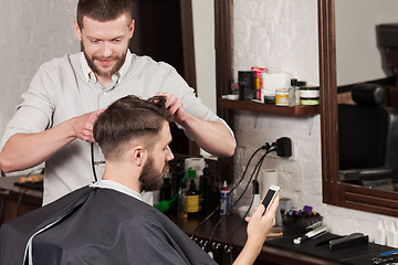 Image showing Young handsome barber making haircut of attractive man in barbershop