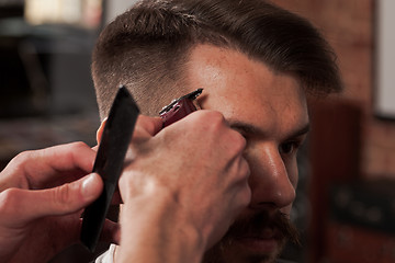 Image showing The hands of barber making haircut to young man in barbershop