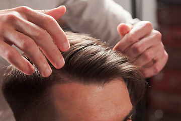 Image showing The hands of barber making haircut to young man in barbershop