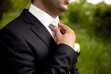 Image showing The groom in a suit, corrects a tie with his hand.