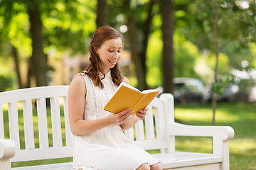 Image showing smiling young woman reading book at summer park