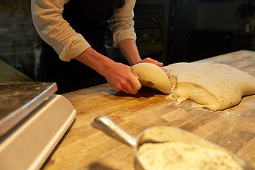 Image showing baker portioning dough with bench cutter at bakery