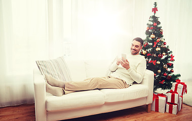 Image showing smiling man with smartphone at home for christmas