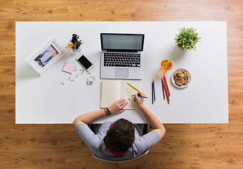 Image showing woman with laptop drawing in notebook at office