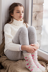 Image showing sad girl sitting on sill at home window in winter
