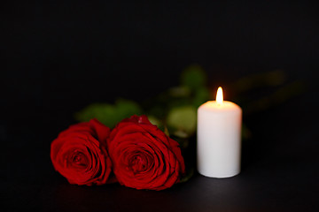 Image showing red roses and burning candle over black background