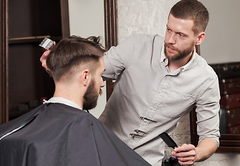 Image showing Young handsome barber making haircut of attractive man in barbershop