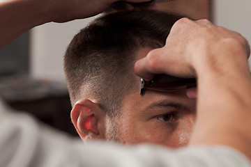 Image showing The hands of barber making haircut to young man in barbershop