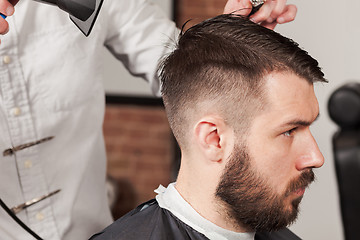 Image showing The hands of barber making haircut to young man in barbershop