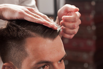 Image showing The hands of barber making haircut to young man in barbershop