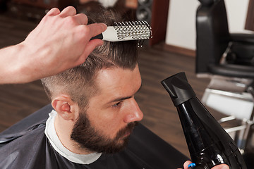 Image showing The hands of barber making haircut to young man in barbershop