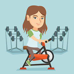 Image showing Young caucasian woman riding stationary bicycle.