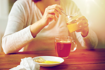 Image showing close up of woman adding honey to tea with lemon