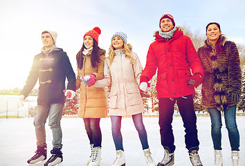 Image showing happy friends ice skating on rink outdoors