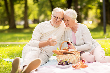Image showing senior couple with smartphone at picnic in park