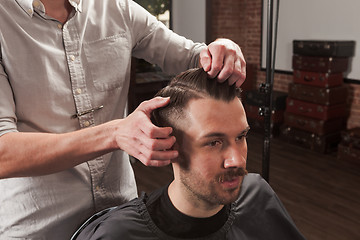 Image showing The hands of barber making haircut to young man in barbershop