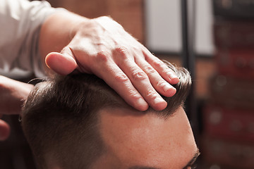 Image showing The hands of barber making haircut to young man in barbershop