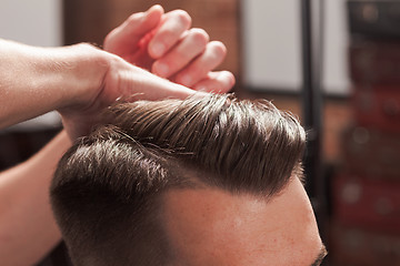 Image showing The hands of barber making haircut to young man in barbershop