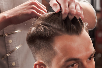 Image showing The hands of barber making haircut to young man in barbershop