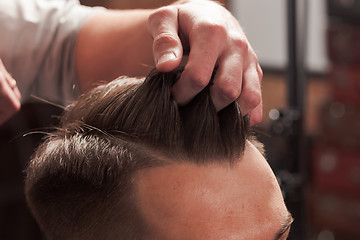 Image showing The hands of barber making haircut to young man in barbershop