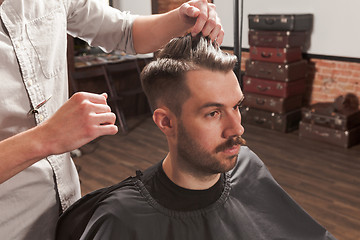 Image showing The hands of barber making haircut to young man in barbershop