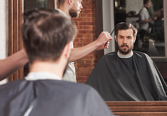 Image showing Young handsome barber making haircut of attractive man in barbershop