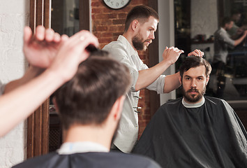 Image showing Young handsome barber making haircut of attractive man in barbershop