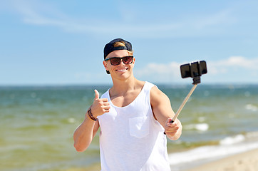 Image showing man with smartphone selfie stick on summer beach