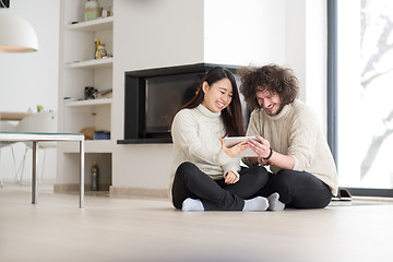 Image showing multiethnic couple using tablet computer in front of fireplace