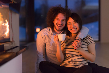 Image showing happy multiethnic couple sitting in front of fireplace