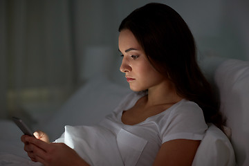 Image showing young woman with smartphone in bed at night