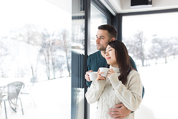 Image showing multiethnic couple enjoying morning coffee by the window