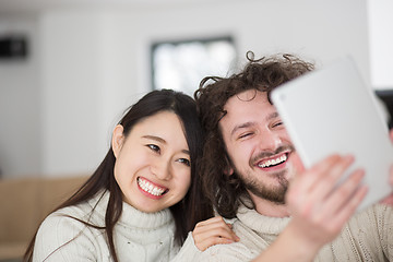 Image showing multiethnic couple using tablet computer in front of fireplace