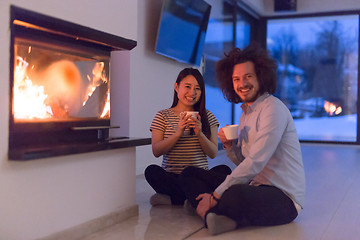 Image showing happy multiethnic couple sitting in front of fireplace