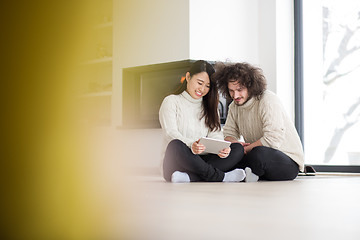 Image showing multiethnic couple using tablet computer in front of fireplace